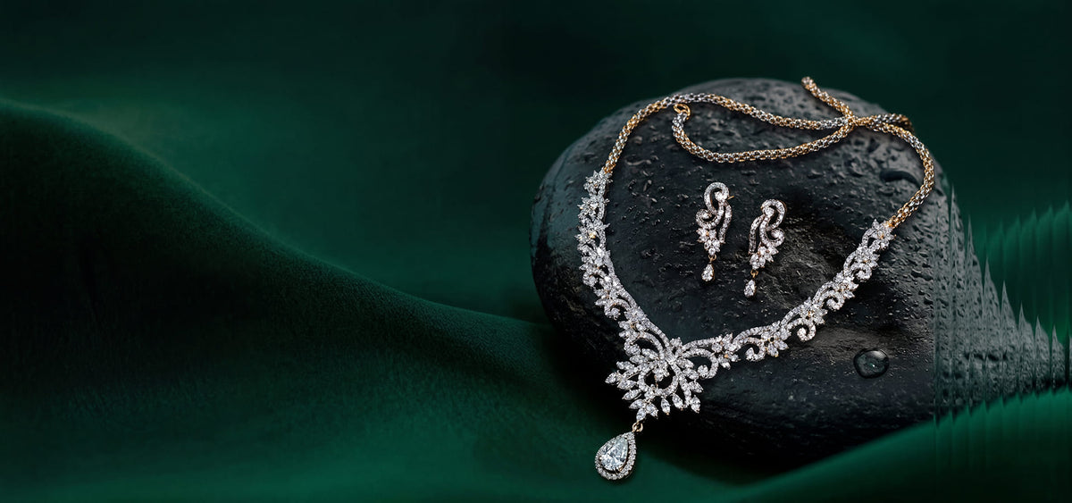 Silver necklace and earrings set on a dark stone with a green fabric background